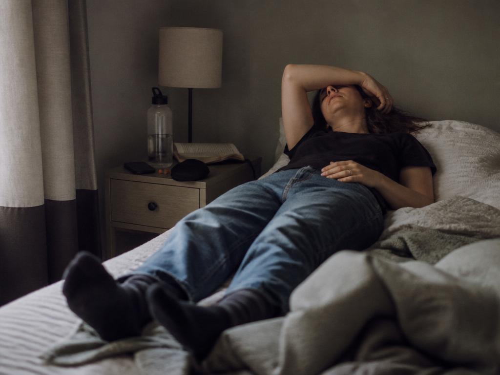 A person resting under a rumpled clay-and-cream duvet in soft late-afternoon light, seen from behind